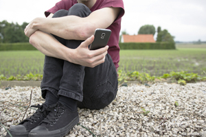 anonymous man outside holding phone wonders if he should call a helpline